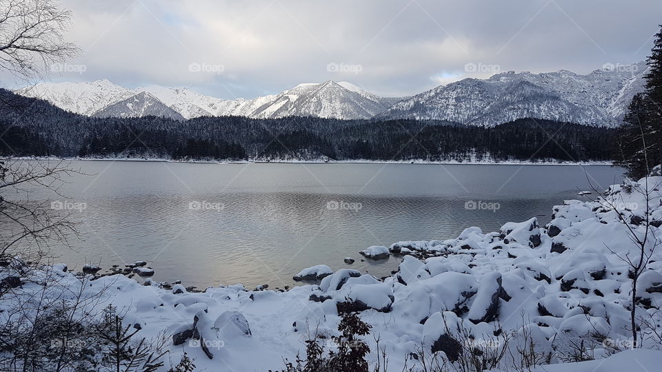 The snow covered landscape of Eibsee, Germany with the sun fighting to break through the overcast sky