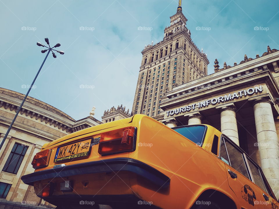 Looking up from the rear of an Old yellow communist style yellow cab and the Palace of Culture and Science in Warsaw.