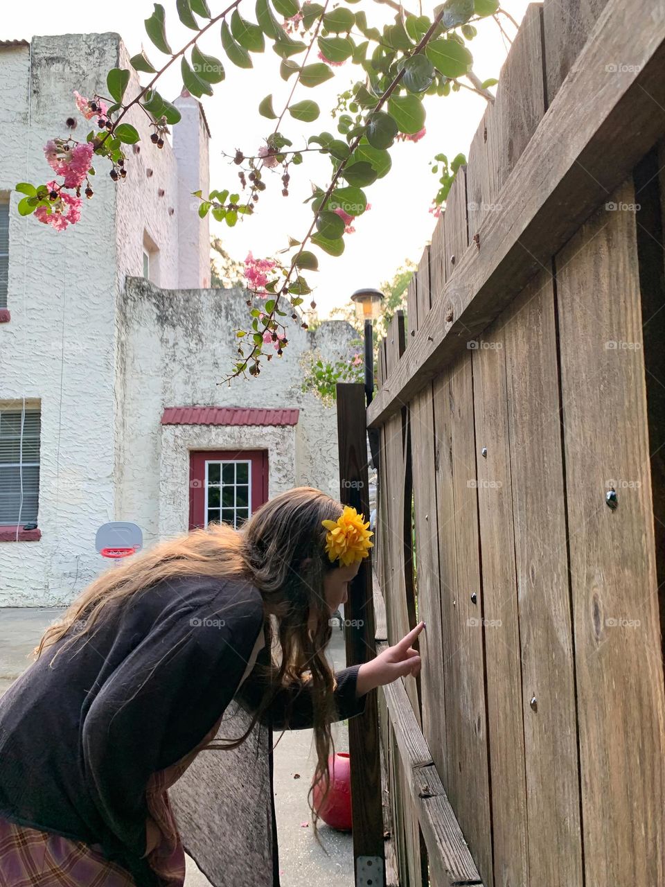 White and red spanish old style architecture residential large house built in the early 1900s. Dark red door and windows with aging signs focusing on tree branch with wet pink flowers and leaves by wooden door with marbles intriguing girl child.