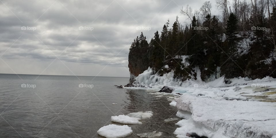 scenic view of a pine covered cliff meeting a calm, frozen lake