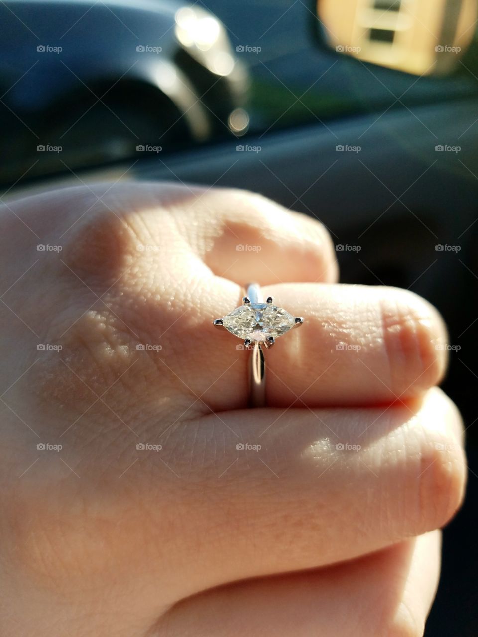 A macro shot of a hand wearing an engagement ring illuminated by sunlight.