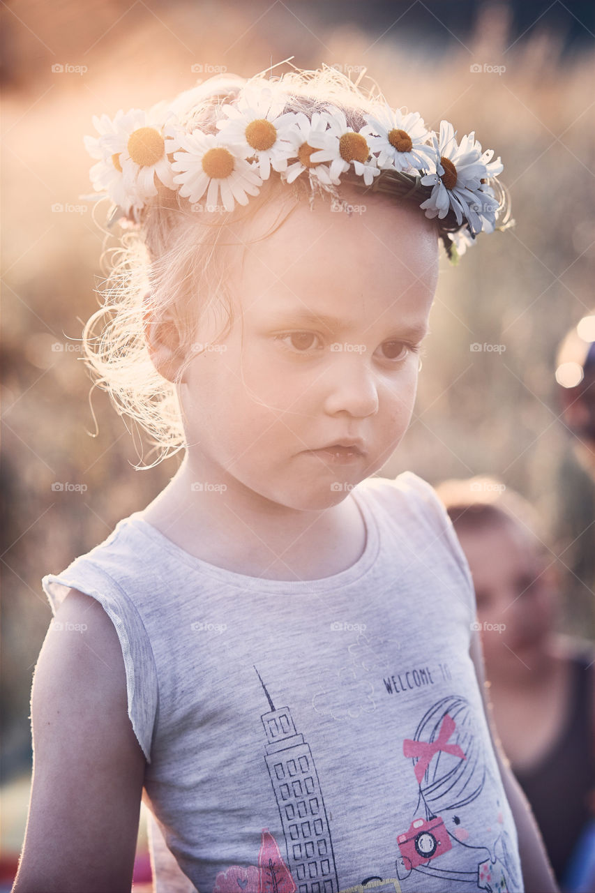 Little girl wearing a coronet of wild flowers on her head. Candid people, real moments, authentic situations