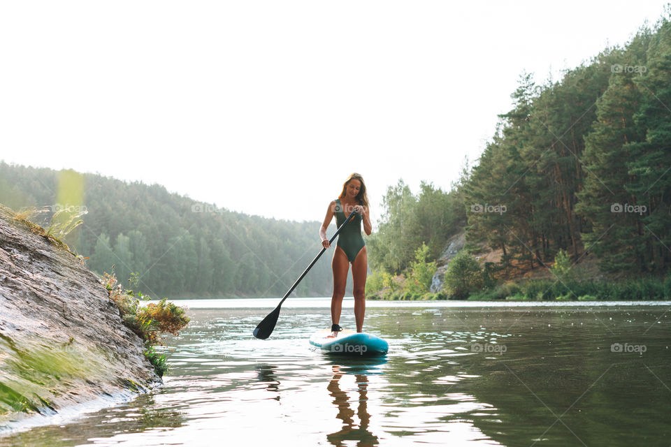 The slim young woman in green sweemsuit on sup boat with oar floating on river, weekend trip and local travel