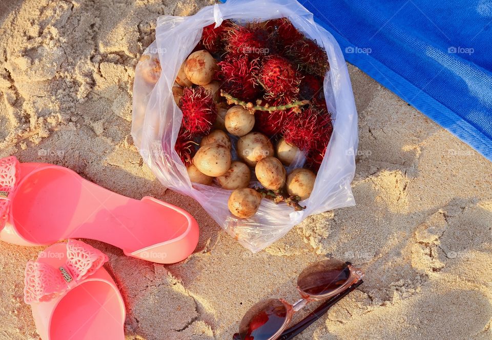 Rambutan fruits with footwears and sunglasses on beach