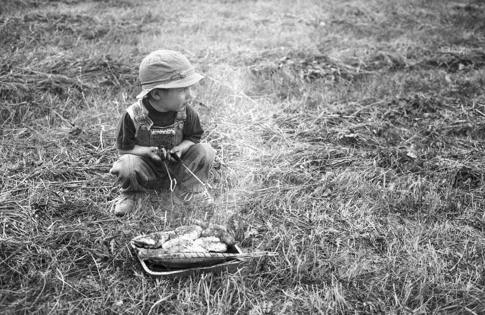 BBQ far away from home. Boy sitting next to BBQ