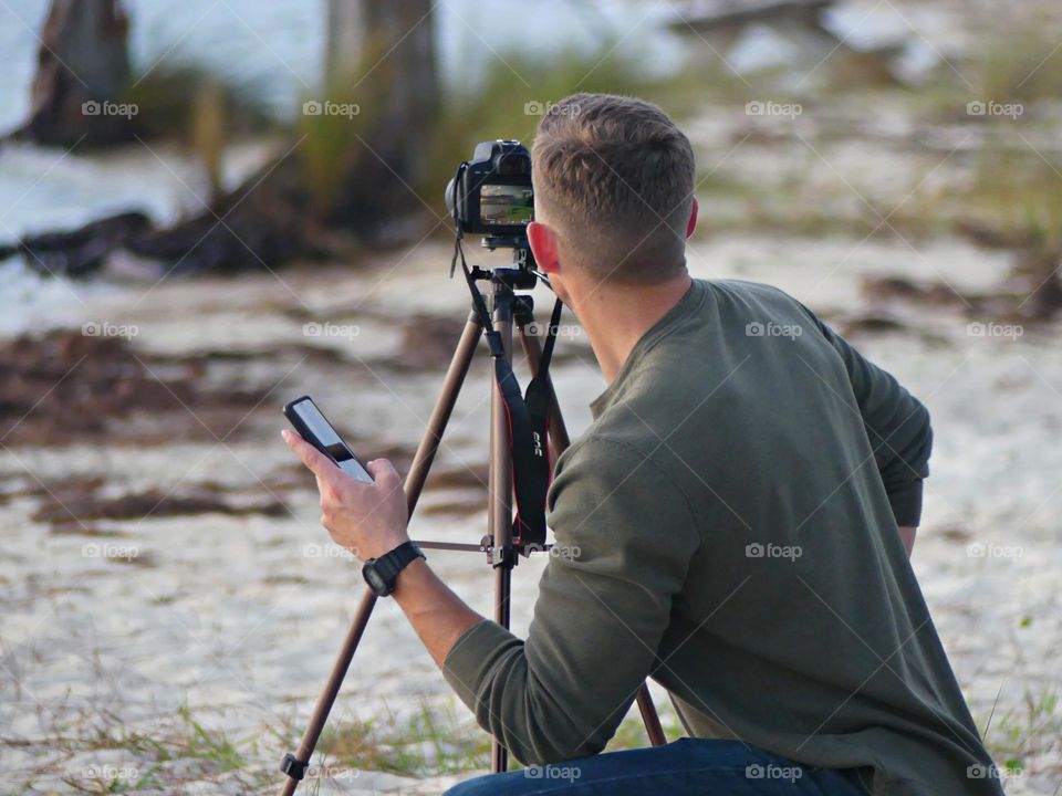 A Video Creator adjusts the settings on his camera during a photo shot of a descending sunset 