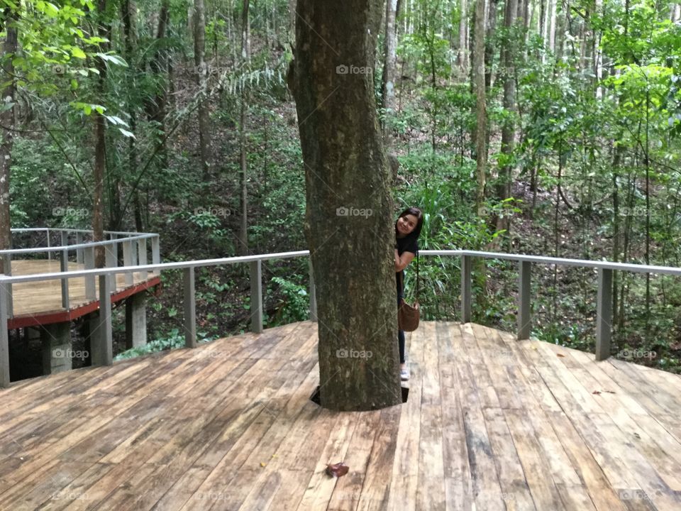  A girl hiding its body half while taking a picture behind a tree trunk.