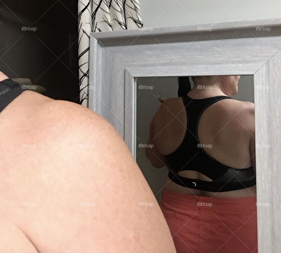 Older, plus size woman, modelling the back of her new black sports bra, and her bare shoulder gets in the way