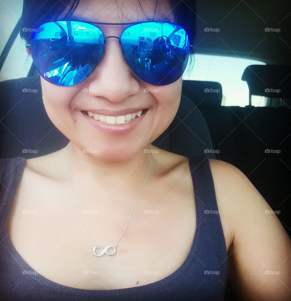 Beautiful lady with sunglasses is making selfie on camera in the car. She is smiling and very happy.