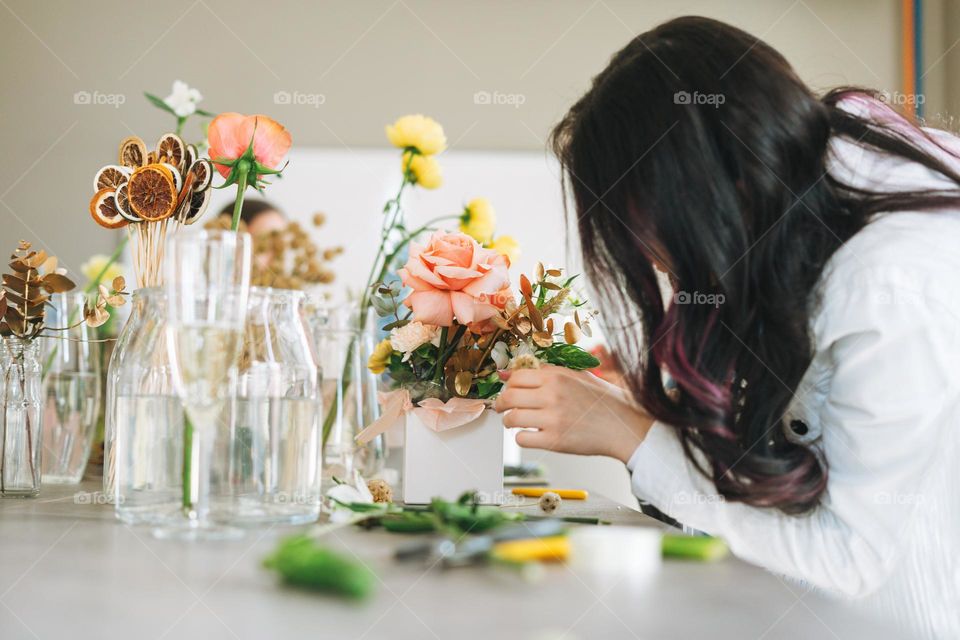 Young woman florist in white with bouquet of flowers in box in flower shop, small local business owner. Young stylish success millennial woman on the creative work