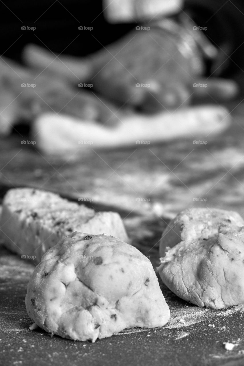 Monochromatic shot of old woman’s hands rolling fresh gnocchi in her kitchen on a floured butcher block. Shows skill, fresh ingredients, finely-honed skills, and cooking with love.