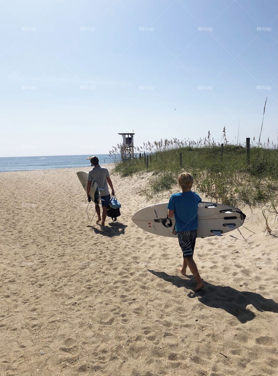 A Father and Son head out onto the beach to do some surfing.