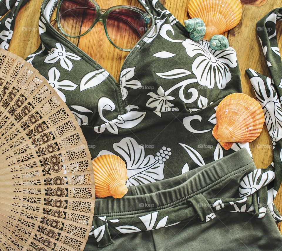 Female swimwear with retro sunglasses, a fan and seashells on a wood background 