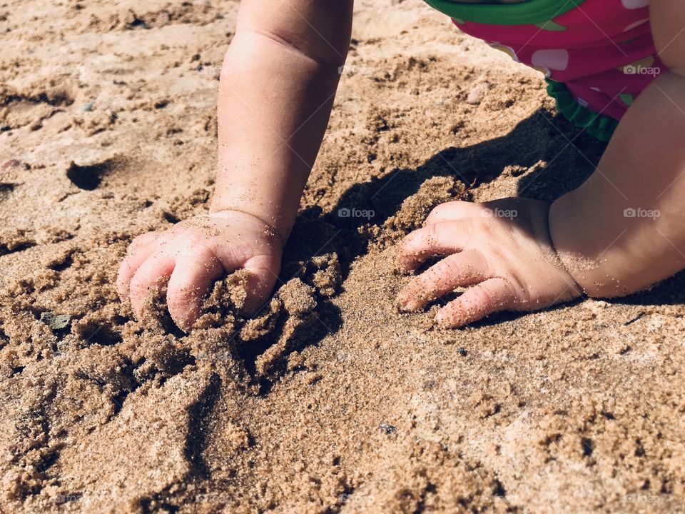 Baby girl digging into sand at a beach