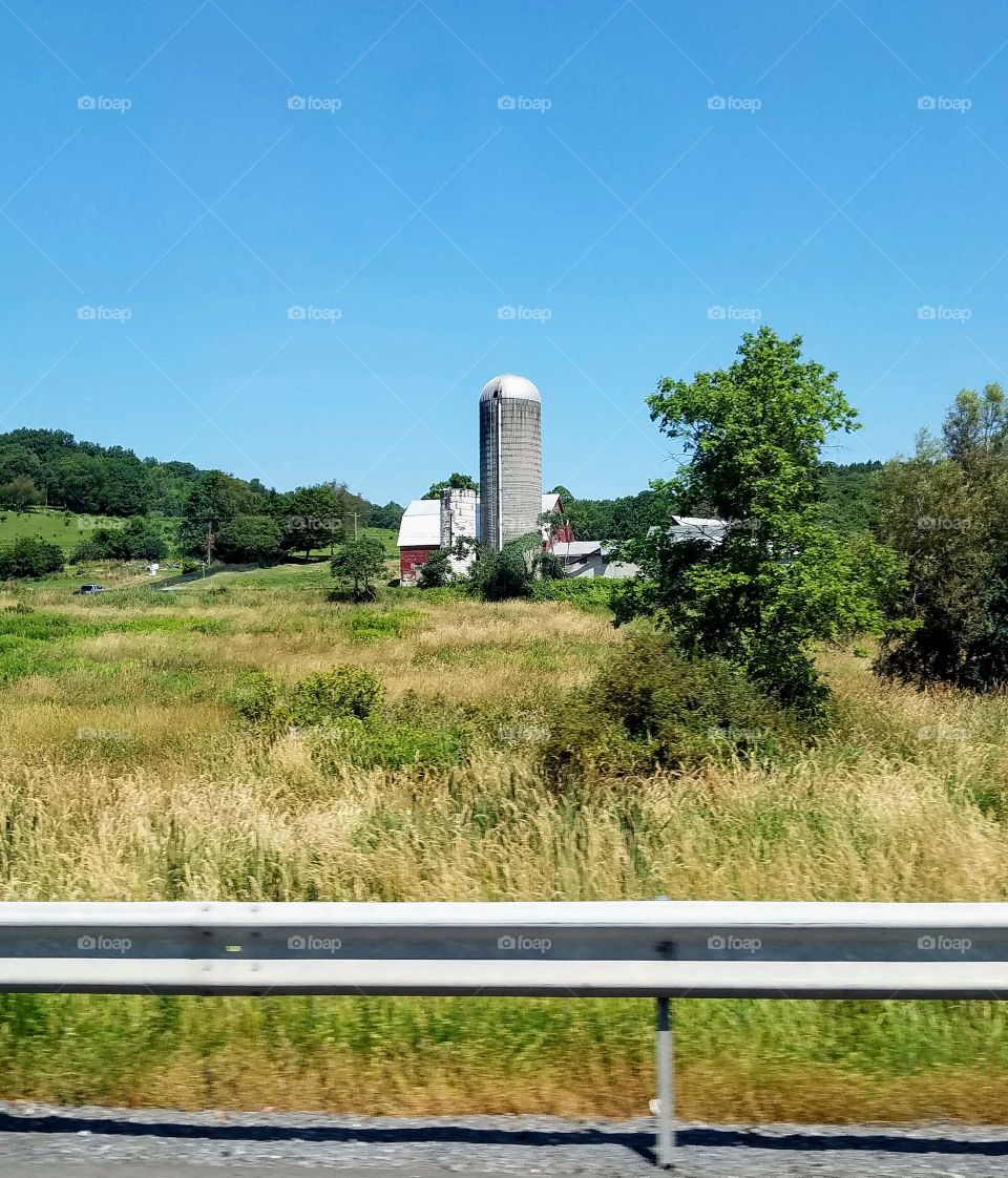 Cities vs Countryside... Here's a peaceful & uncrowded area in the Countryside view from a highway. There's a tall silo, barn & farmhouse with acres of fields around it.
