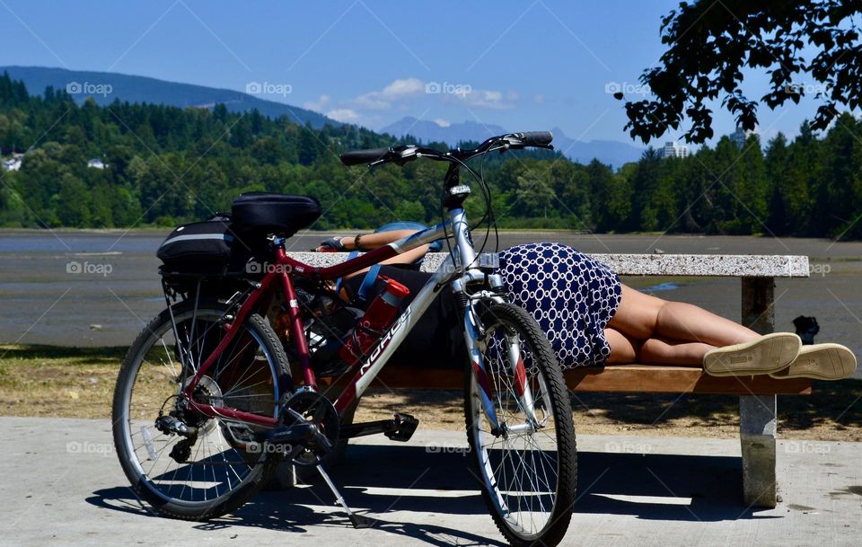 Solitary bicycle bike parked beside a woman sleeping on a bench in summer in British Columbia 