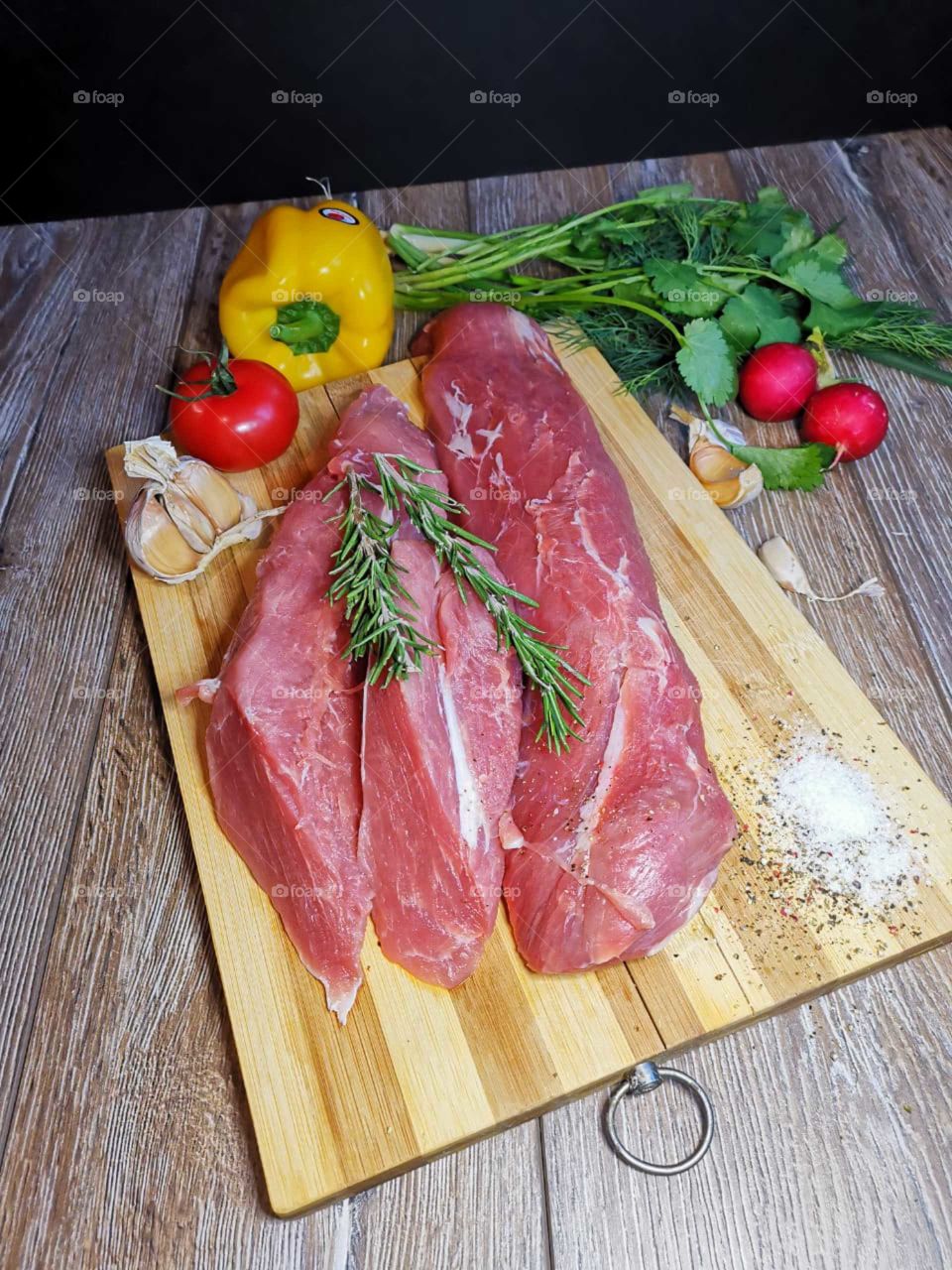 A piece of raw meat on a cutting board, peppers, garlic, tomatoes.