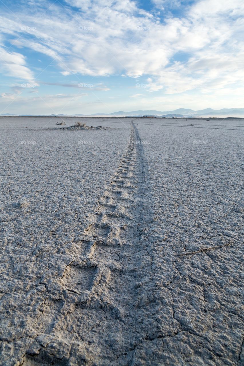 Tire track disappears horizon. Motorcycle tire track disappears to horizon. Bonneville salt flat. Mountains in horizon. Partly cloudy sky