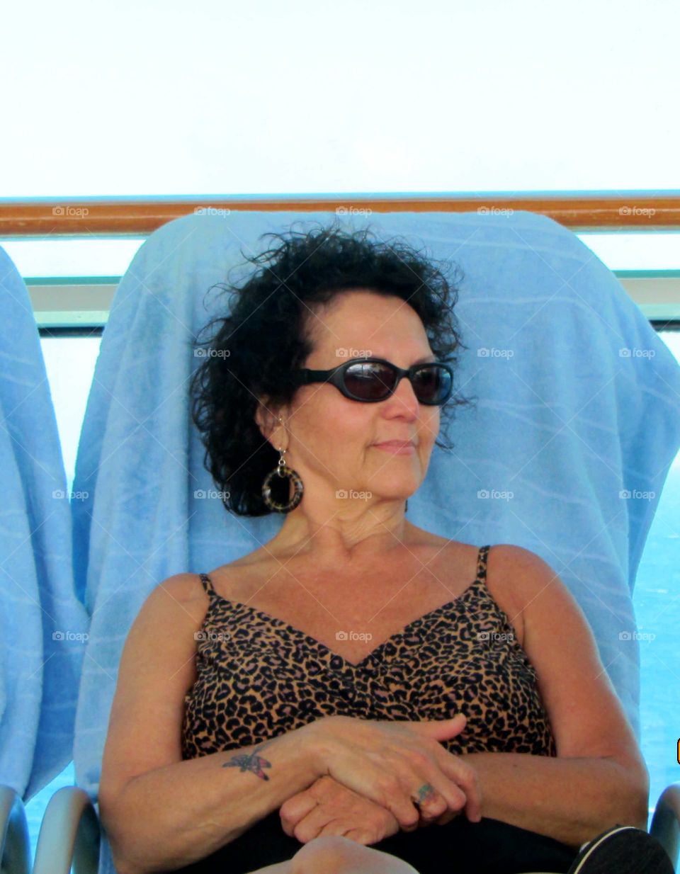 Pic of woman relaxing, smiling as she sits in a lounge chair pool side sunbathing with sunglasses on. She's smiling with contentment. Her bathing suit is leopard print. Wonder what she's thinking about?
