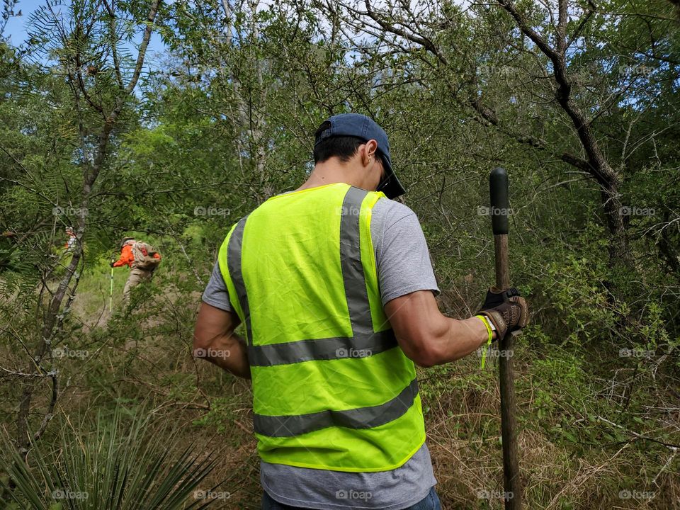 Man with safety vest working in a wooded area.