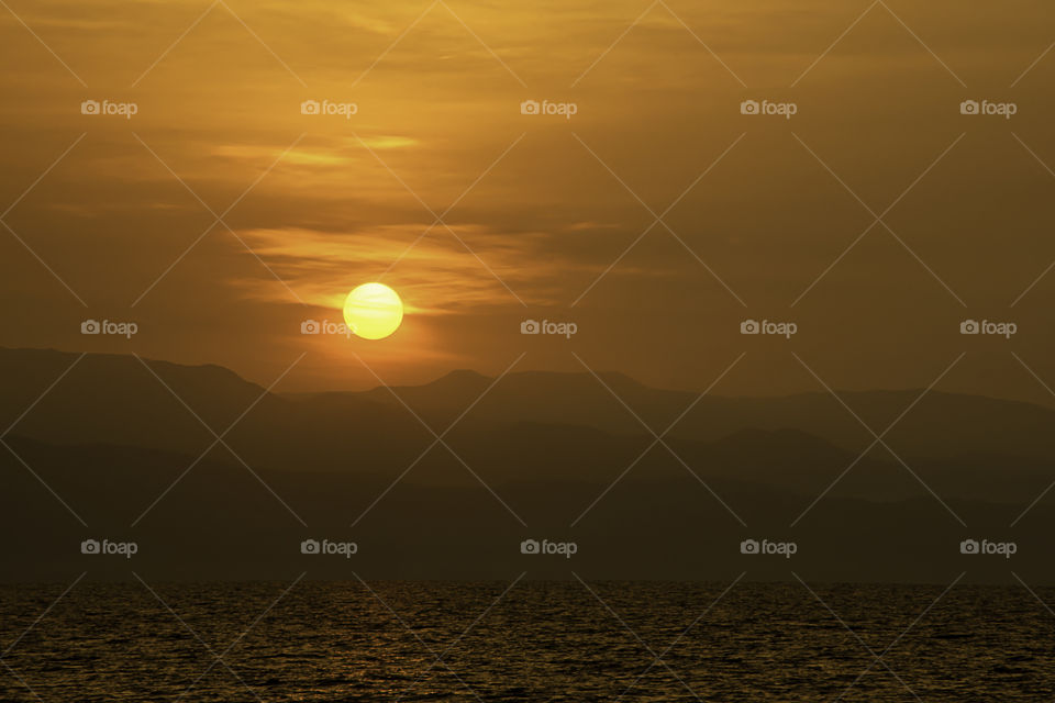 Golden light of sunrise behind the mountains and the sea.