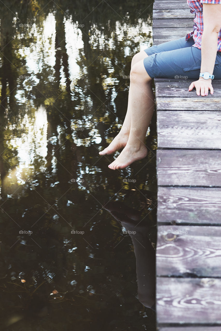 Woman sitting on a bridge over a lake, among the trees, close to nature, during summer vacations. Candid people, real moments, authentic situations