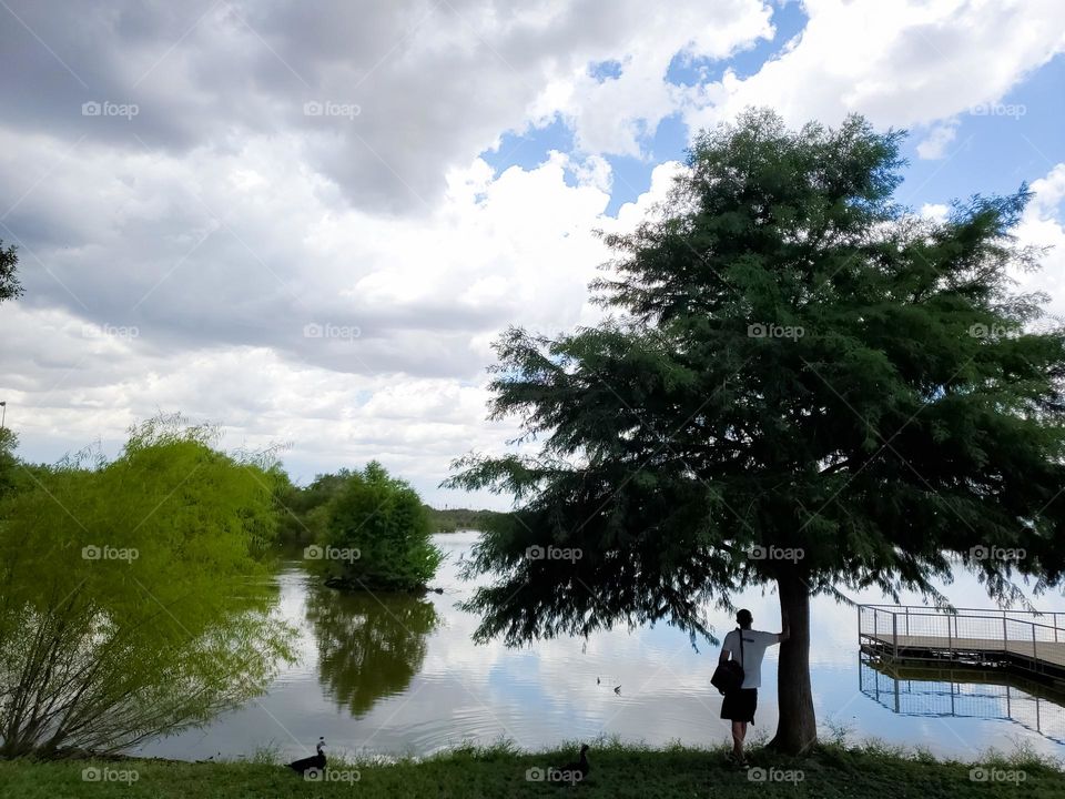 A man leaning on a tree enjoying a peaceful, quiet moment by the lake.