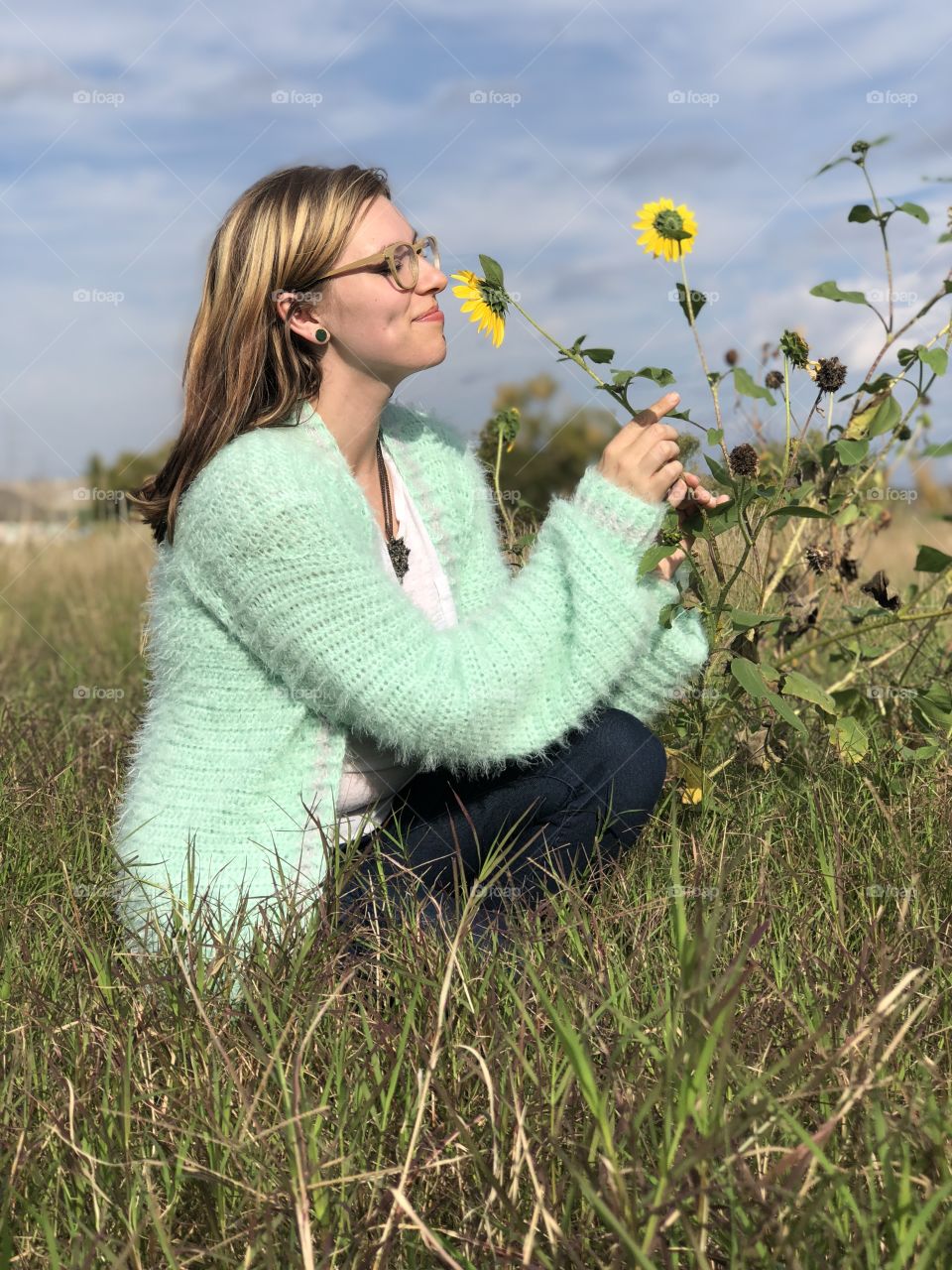 Beautiful lady stopping to smell the sunflowers in a field