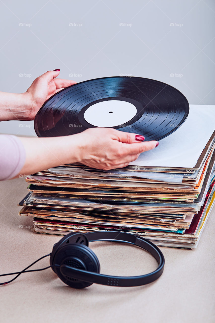 Woman taking vinyl from stack of many black vinyl records, headphones put at the front of vinyls. Copy space for text. Candid people, real moments, authentic situations