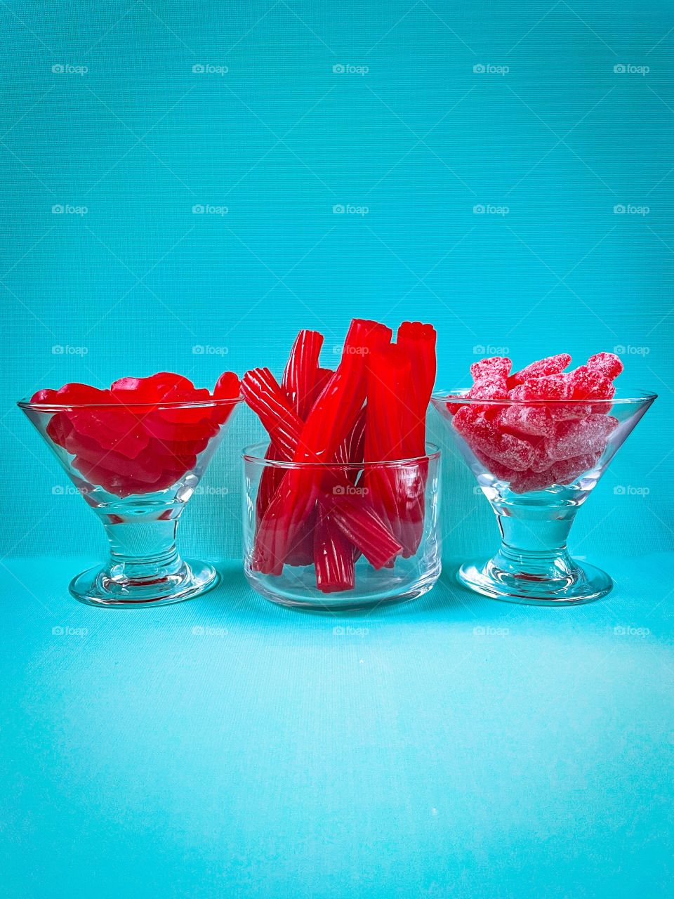 Three clear dishes filled with red gummy candy with blue background. 