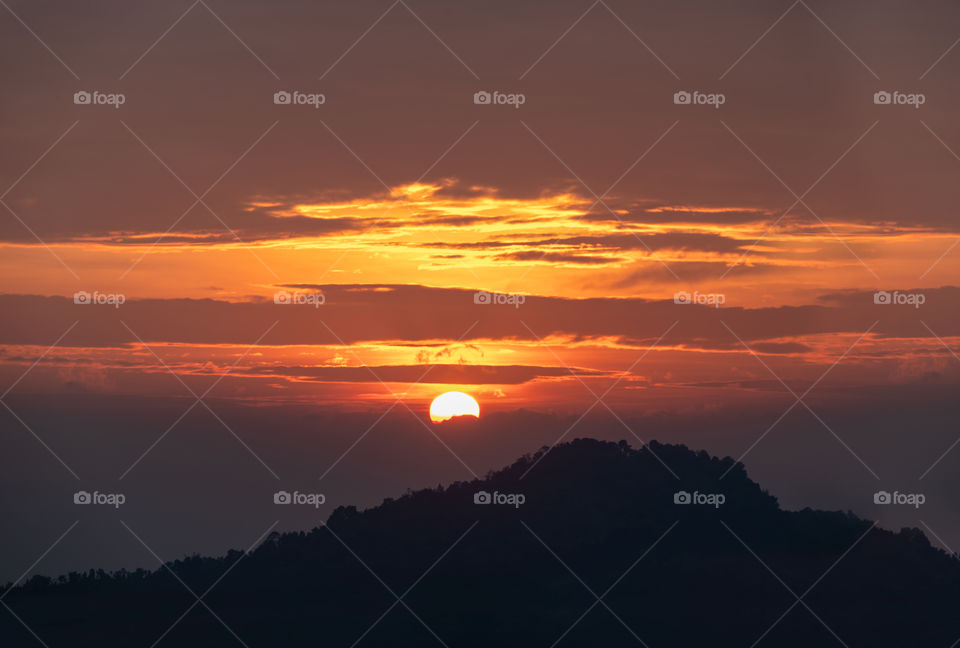 Sunrise above silhouette of big mountain