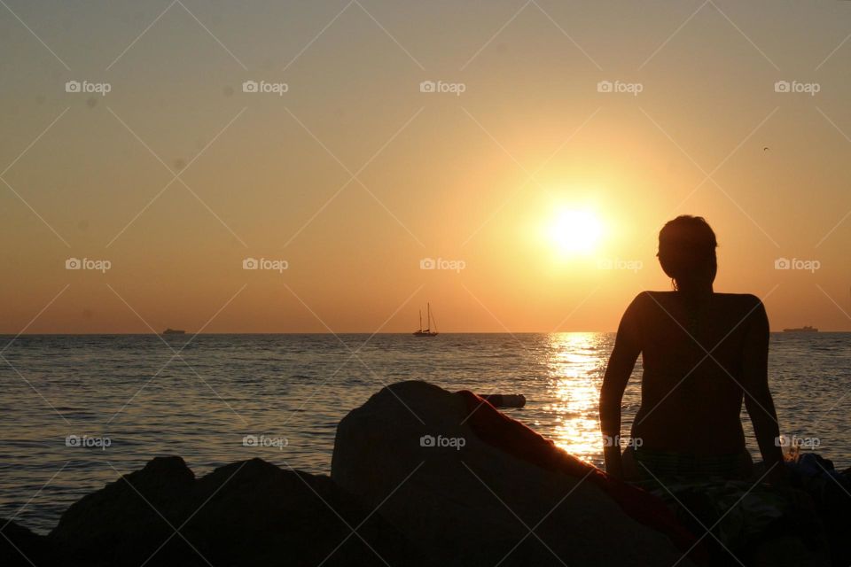 Man sitting on the rocks by the sea watching sunset 