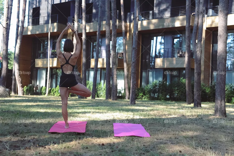 a girl in a black tracksuit, on a pink rug in the forest, does yoga, the girl meditates
