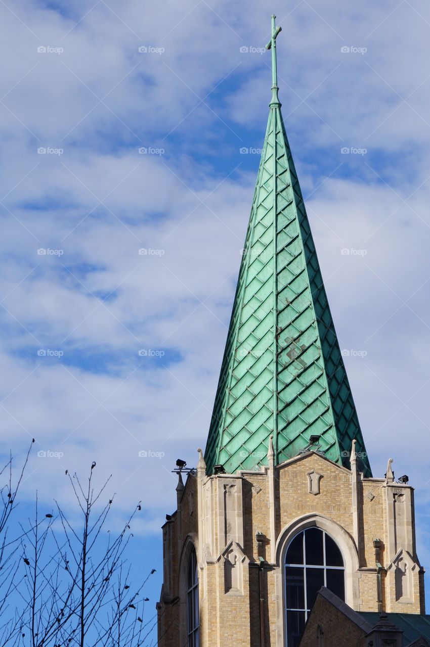 Church spire. Photo taken in downtown Tulsa of green patina on church steeple reaching into a blue sky with white fluffy clouds.